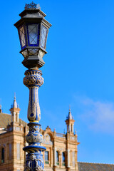 Fototapeta na wymiar Ceramic tiled lantern and Plaza de Espana ancient architecture on background against blue sky. Beloved famous touristic place, main landmark of Sevilla city Andalusia, Spain