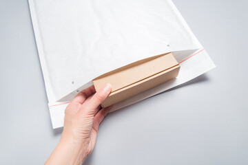 Hand put brown cardboard box to white bubble envelopes on grey background