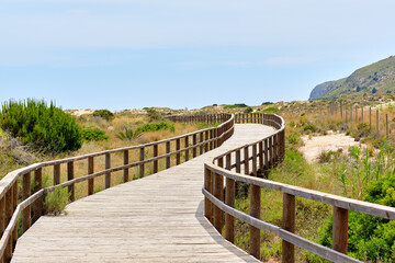 Fototapeta na wymiar Wooden empty board walk leading through sandy dunes to Mediterranean Sea and beach of Los Arenales del Sol or Arenals del Sol. Costa Blanca, Europe, Spain. Espana