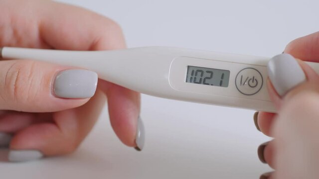 Slow motion: woman hands holding white digital medical thermometer with high temperature on table - close up view, selective focus. Healthcare, measurement, disease, infection, coronavirus concept