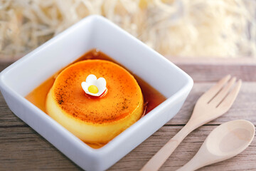 Homemade caramel custard pudding on white plate with wood background