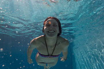 A girl swimming in the pool and diving in the pool, enjoying the pool and the summer. The girl is diving in the pool and is wearing a bikini, and she is holding a breath