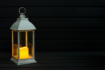 Yellow candle lighting in white lantern on the dark wooden background, space for text