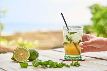 Mojito ready to drink with the beach in the background. Drinking concept for summer.