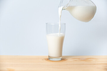 Hand holding jar with fresh milk pouring into glass on wooden table 