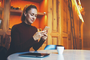 Beautiful woman posing while sitting with touch pad in modern coffee shop interior during work break