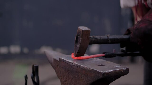 Super slow motion: professional blacksmith showing how to work with metal on anvil at summer handicraft festival - close up view. Handmade, learning, education, craftsmanship and blacksmithing concept
