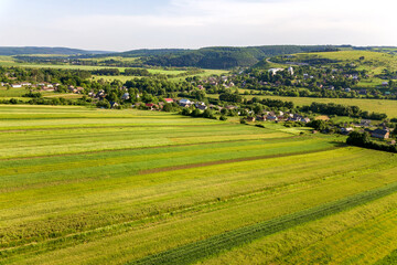 Obraz premium Aerial view of a small village win many houses and green agricultural fields in spring with fresh vegetation after seeding season on a warm sunny day.