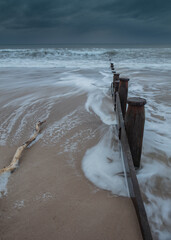 Incoming waves at a wooden groyne on Blyth Beach on the coast of Northumberland, England, UK. With brooding, stormy blue sky overhead.