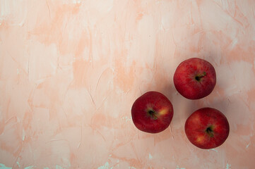 top view of three red whole ripe apples on a light pink background. space for text