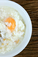 Homemade Thai Rice Soup With chicken, pork and Soft boiled egg or onsen egg in white blow on rustic wooden background. Thai style Food. Top view.