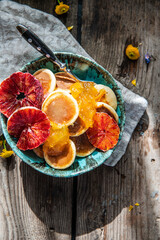 Ceramic bowl with mini pancakes, blood orange slices, orange jam and honey on old wooden table.