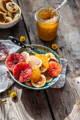 Ceramic bowl with mini pancakes, blood orange slices, orange jam and honey on old wooden table.