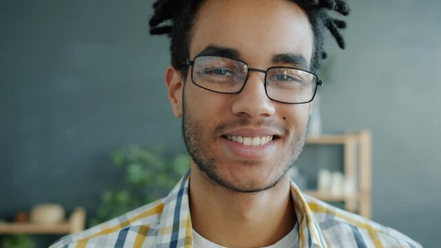 Close-up portrait of Afro-American guy smiling and looking at camera indoors in house against dark gray wall. People and positive emotions concept