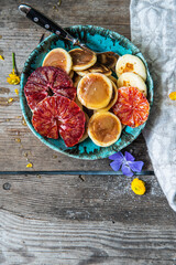 Ceramic bowl with mini pancakes, blood orange slices and honey on old wooden table.