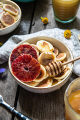 Ceramic bowl with mini pancakes, blood orange slices and honey on old wooden table.