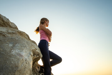 Naklejka na ściany i meble Woman hiker leaning on a big rock enjoying warm summer day. Young female climber resting during sports activity in nature. Active recreation in nature concept.