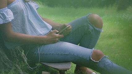 CU PAN SLO MO Woman sitting against tree and using smartphone / Hackney, London, England, UK