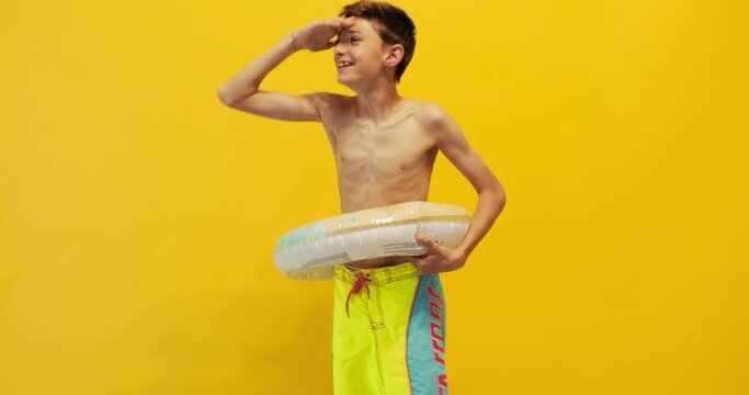 Happy teen guy, standing with an inflatable sea circle and celebrating victory, isolated on a yellow background