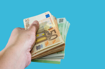 Banknotes of 50 and 100 euros in a human hand on a blue background. Much money. Financial concept. Copy of space.