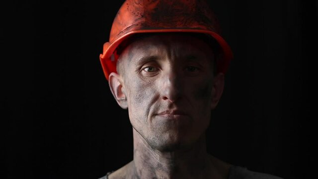 The face of a male miner in a helmet on a black background. Portrait of a mining worker.