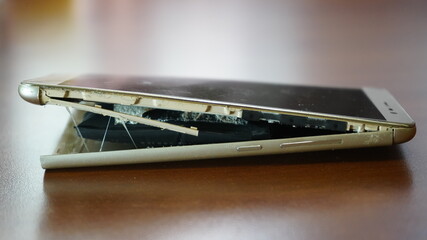 Swollen smartphone battery. Damaged smartphone with a faulty battery. Damaged phone on a wooden background.