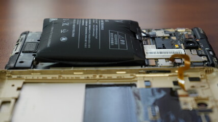 Swollen smartphone battery. Damaged smartphone with a faulty battery. Damaged phone on a wooden background.