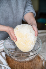 Step by step process of making yeast bread.  woman hands holding dough above glass bowl.