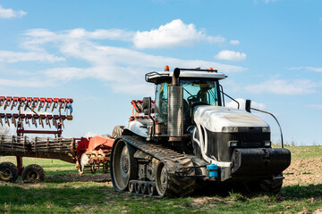 A very large white crawler tractor stands in a field in summer while cultivating agricultural land
