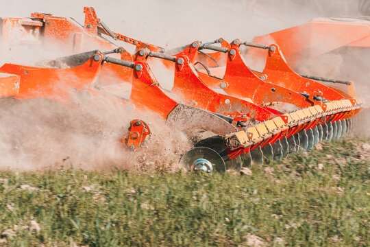 Agricultural equipment shreds the plowed land. A crawler tractor pulls a harrow to loosen the soil close up.