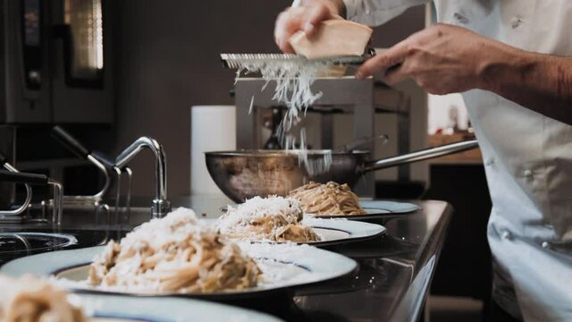 MS TS Chef grating parmesan cheese on spaghetti on plates / Florence, Tuscany, Italy