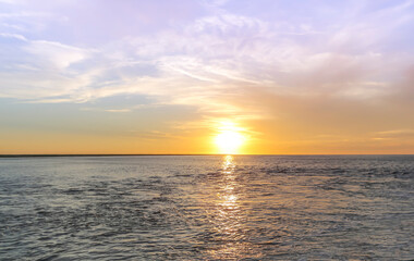 Naklejka na ściany i meble Bright yellow sunset across flat ocean with small ripples