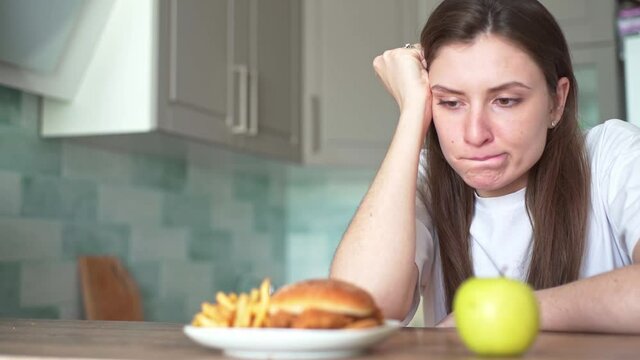 A young woman suffers because of the choice of food between harmful and healthy. The temptation to eat a hamburger with fried fries, dieting