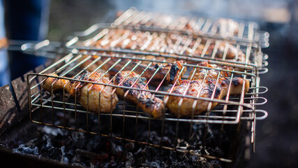Chicken thighs and chicken breast are fried on an outdoor fire on a metal grid.