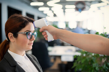 Temperature measurement by electronic infrared thermometer for office staff. Sick woman in a suit....