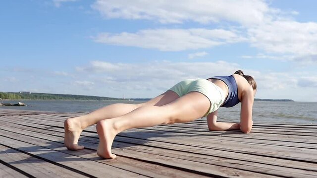 Sports girl goes in for sports on the street near the sea. Youth and sports concept. Online training, tabata, outdoor sports, outdoor sports