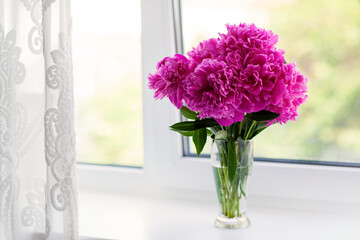 A beautiful bouquet of pink peonies stands on the windowsill