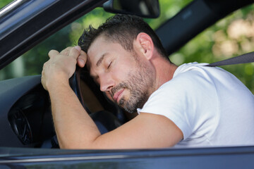 man asleep leaning over the steering wheel of his car