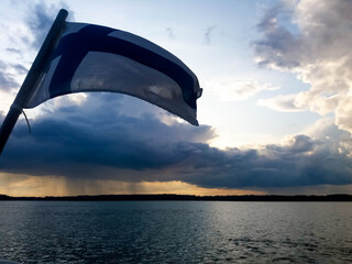 The flag of Finland flying with the wind on a boat near Helsinki. On a horizon there is a rain shower and dark clouds.