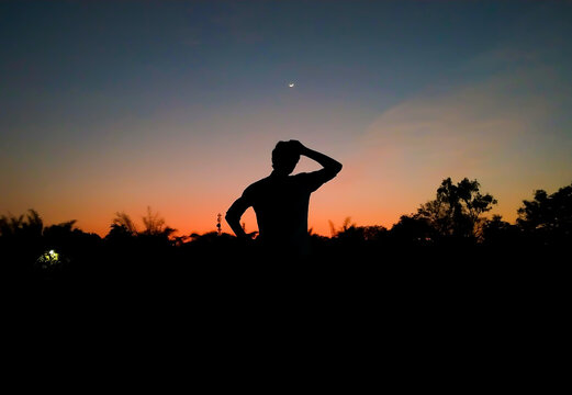Silhouette of a boy scratching his head in confusion and thinking in the evening with crescent moon in the sky after sunset as background. Inspirational. De clutter mind concept. Depression.