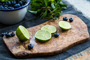 Sliced key lime and few blueberries on wooden board on  dark background.