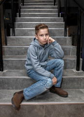 A boy with trimmed stripes on his head in a gray hoodie on the stairs