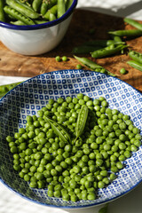 Fresh green pea in blue and white plate and pea pods in white metal ladle on wooden board  on white background.