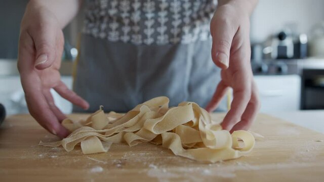 Woman picking up fresh tagliatelle Pasta, at home on a worktop kitchen.