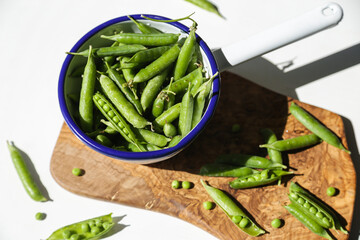 Green pea pods in white metal ladle on wooden board  on white background.