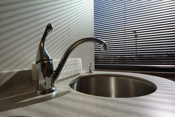 A kitchen faucet near a window in the late afternoon shadows.