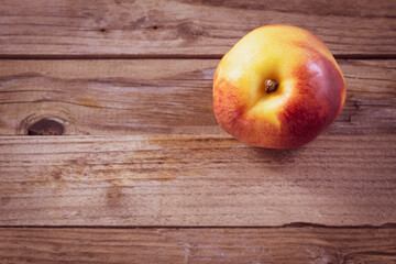 One fresh nectarine lies on wooden boards
