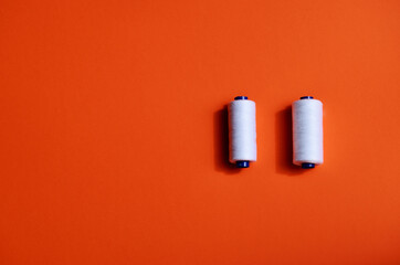Two coils with a white sewing thread lie on an orange background with a copy space