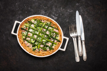 Decorated tarte with Asparagus. Open pie with asparagus cheese bacon and eggs in baking dish on black background.