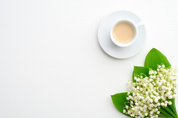 Mug of coffee and spring flowers lily of the valley on white background. Top view with copy space....